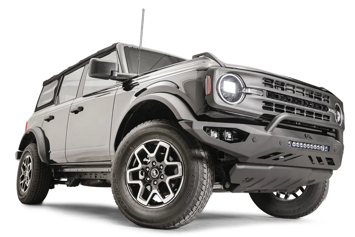 Fab Fours Vengeance front bumper with pre-runner guard on a black Ford Bronco, front passenger-side three-quarter studio view, showing the pre-runner hoop, light bar and skid plate