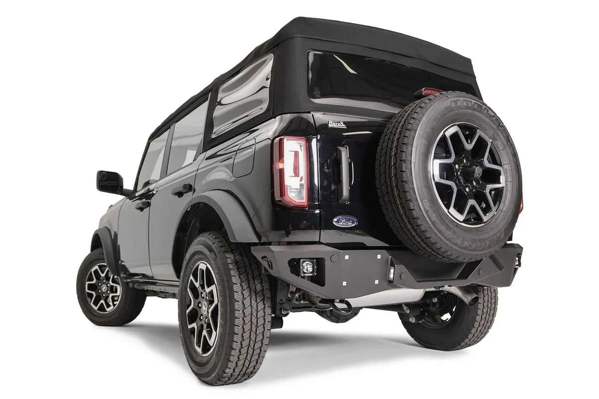 Fab Fours Vengeance rear bumper with cube lights on a black Ford Bronco with soft top and tailgate-mounted spare tire, driver-side rear three-quarter view