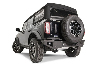 Fab Fours Vengeance rear bumper with cube lights on a black Ford Bronco with soft top and tailgate-mounted spare tire, driver-side rear three-quarter view