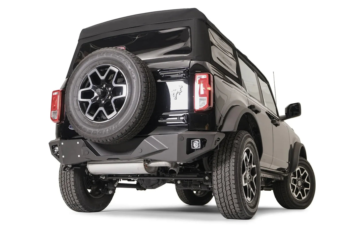 Fab Fours Vengeance rear bumper with cube lights on a black Ford Bronco with soft top and tailgate-mounted spare tire, passenger-side rear three-quarter view