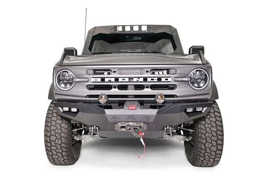 Fab Fours Lifestyle winch front bumper on a lifted gray Ford Bronco, front view, with Warn winch, D-ring shackles, two round pod lights, dual cube lights in each corner, and parking sensors