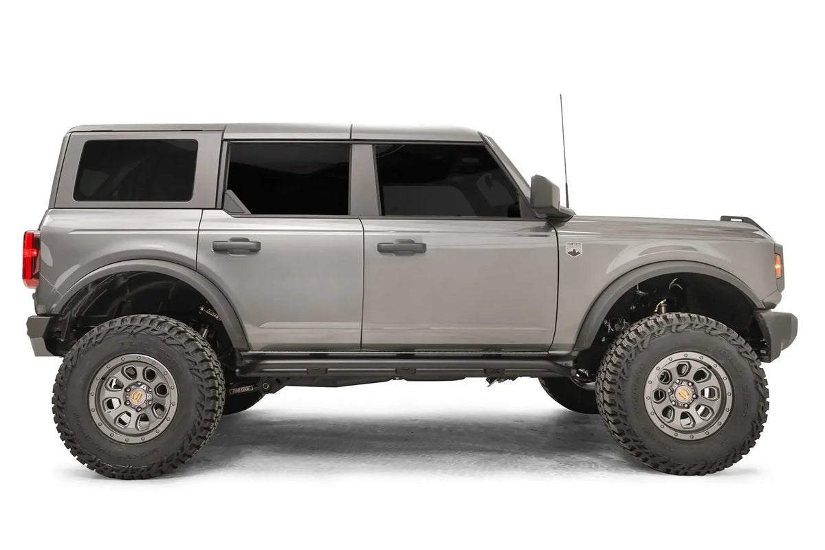Fab Fours rock slider on a gray four-door Ford Bronco, passenger-side profile, with the low-profile black slider running between the wheels beneath both doors