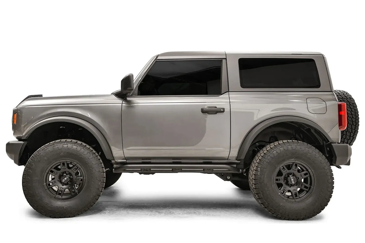 Fab Fours rock slider on a gray two-door Ford Bronco, driver-side profile, with the low-profile black slider running between the wheels beneath the door