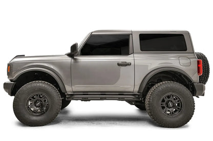 Fab Fours rock slider on a gray two-door Ford Bronco, driver-side profile, with the low-profile black slider running between the wheels beneath the door