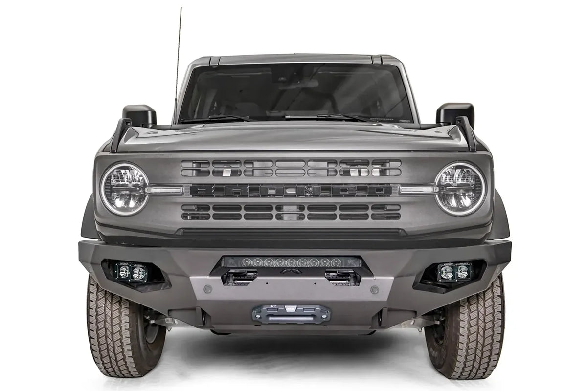 Fab Fours Matrix front bumper on a gray Ford Bronco, straight-on front studio view, showing the full-width bumper, top light bar, winch fairlead and cube light pods