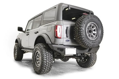 Fab Fours tire carrier relocation bracket on a gray four-door Ford Bronco, rear driver-side view, with the spare tire mounted on the tailgate above a Fab Fours rear bumper