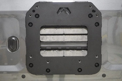 Close-up of the Fab Fours tire carrier relocation bracket bolted to a Ford Bronco tailgate, showing the matte black steel plate with Fab Fours logo cutout and mounting holes