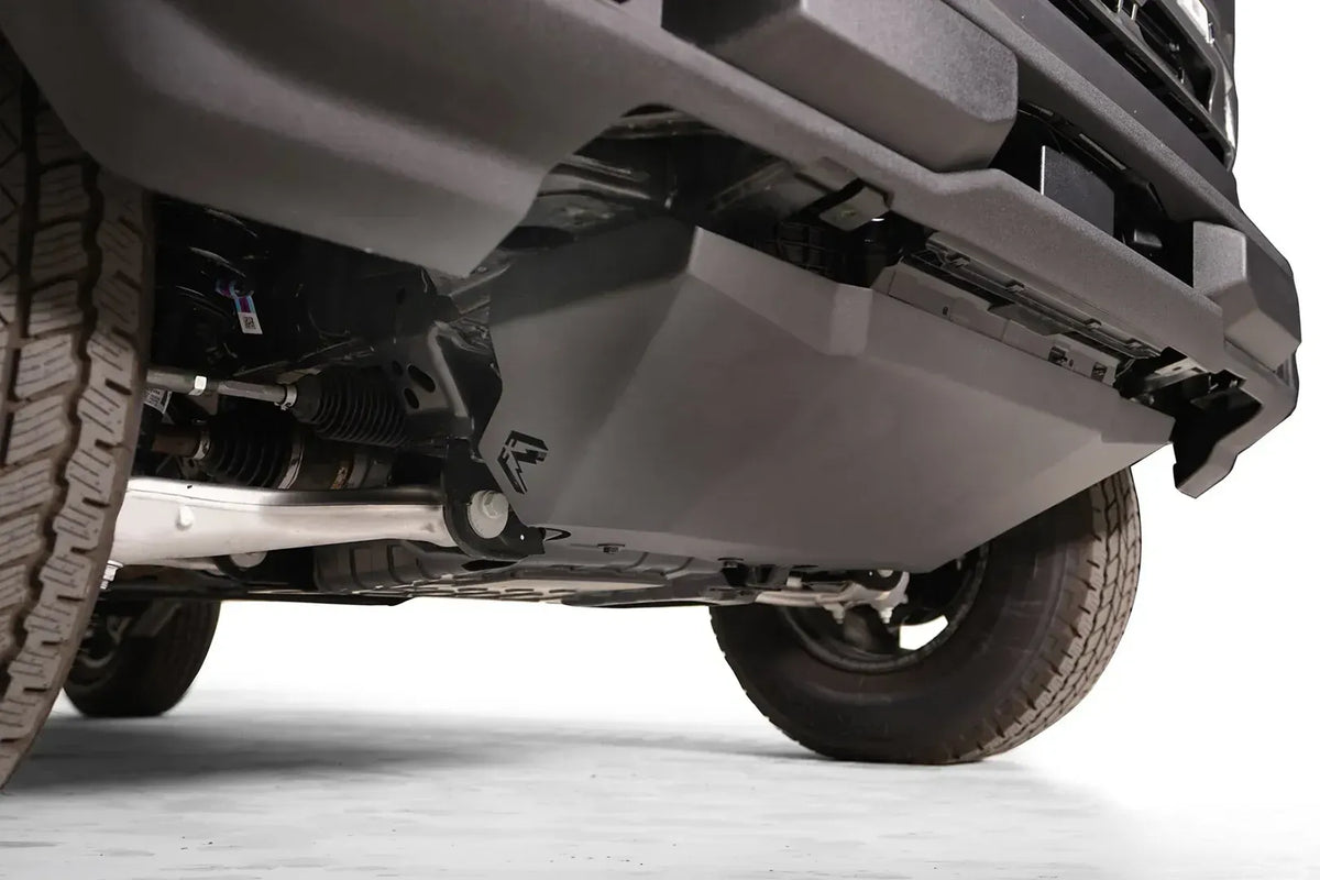 Fab Fours engine skid plate on a Ford Bronco, low close-up from the driver side, showing the angled black steel plate, the Fab Fours logo and the bolt-on mounting below the front bumper