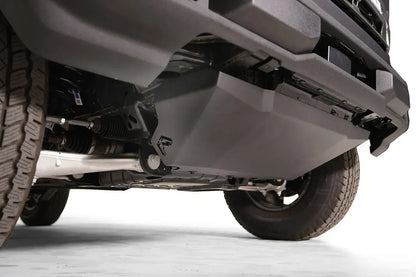 Fab Fours engine skid plate on a Ford Bronco, low close-up from the driver side, showing the angled black steel plate, the Fab Fours logo and the bolt-on mounting below the front bumper