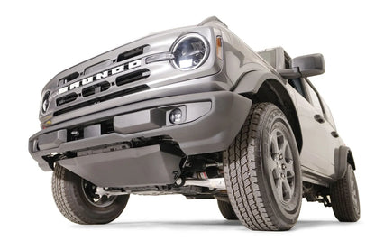 Fab Fours engine skid plate on a gray Ford Bronco with the factory front bumper, low front driver-side view, showing the black skid plate with the Fab Fours logo covering the engine below the bumper