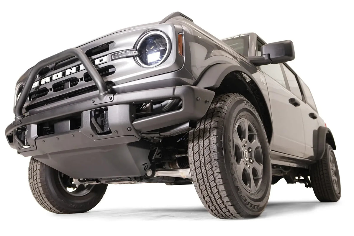 Fab Fours engine skid plate on a gray Ford Bronco fitted with a Fab Fours front bumper with pre-runner hoop, low front driver-side view, showing the skid plate tucked beneath the bumper