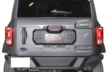 Close-up of the Fab Fours spare tire delete plate on a Ford Bronco tailgate, showing the slotted accessory mounting holes, license plate area and raised third brake light