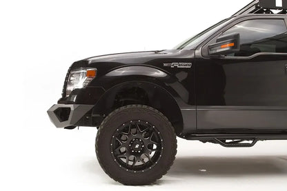 Fab Fours Vengeance front bumper on a black Ford F-150, close-up of the driver-side bumper end, showing the angular end cap and tire clearance