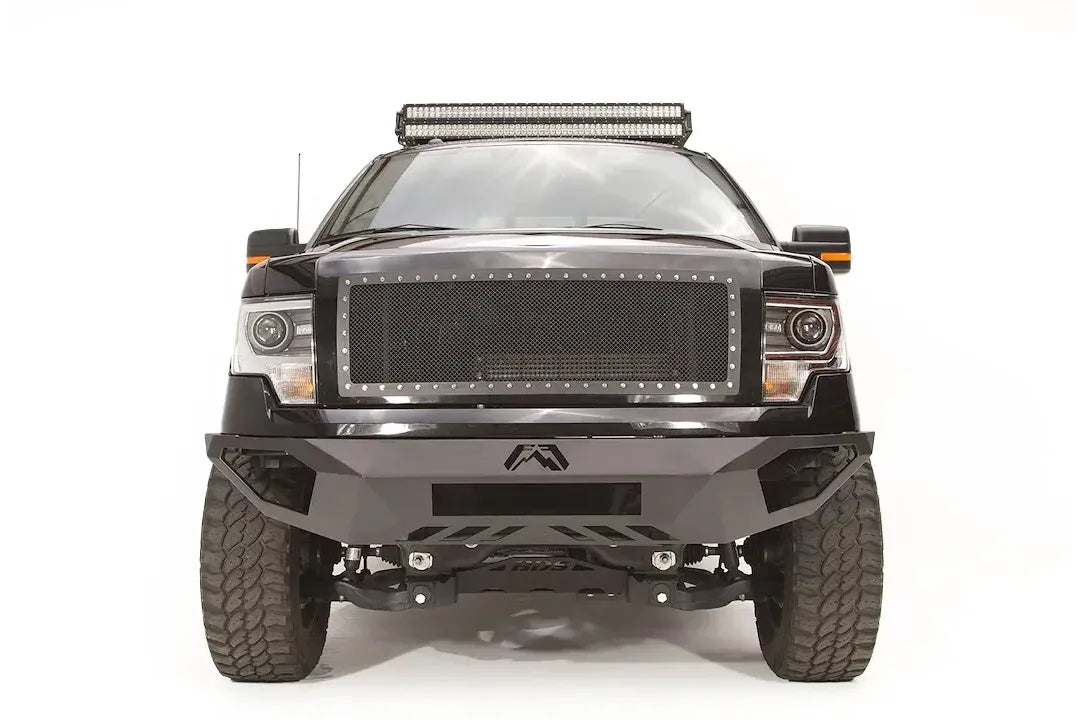 Fab Fours Vengeance front bumper on a black Ford F-150, straight-on front studio view, showing the sculpted bumper face, center logo plate and lower skid section