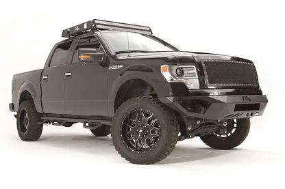 Fab Fours Vengeance front bumper on a black Ford F-150, front passenger-side three-quarter studio view, showing the low-profile bumper, end caps and center logo plate