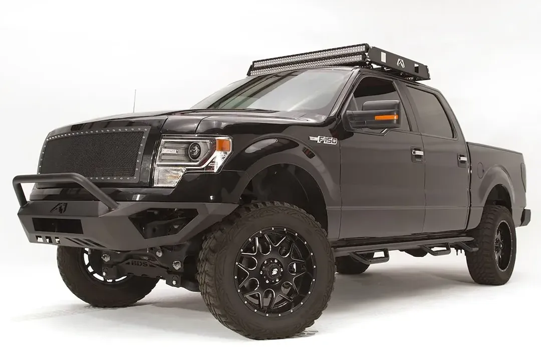 Fab Fours Vengeance front bumper with pre-runner guard on a black Ford F-150, front driver-side three-quarter studio view, showing the pre-runner hoop, bumper wing and lower skid section