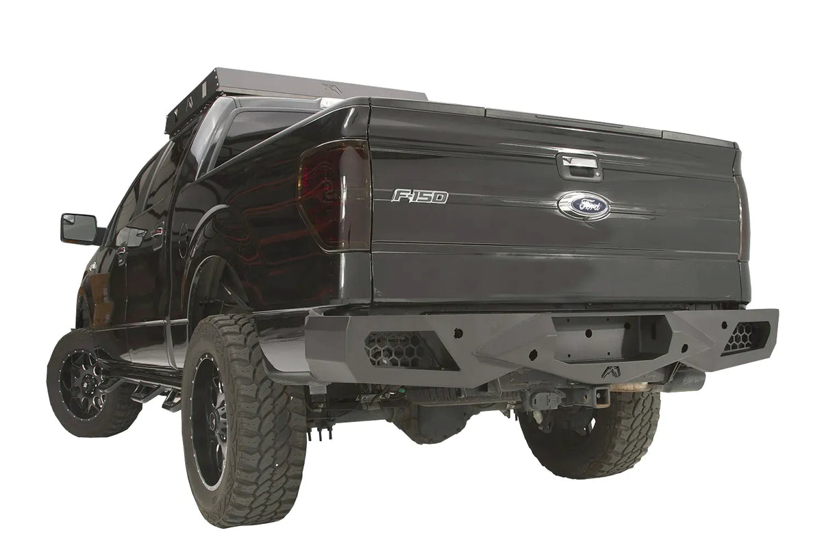 Fab Fours Vengeance rear bumper on a black Ford F-150, rear driver-side three-quarter studio view, showing the sculpted bumper, honeycomb corner vents and hitch receiver