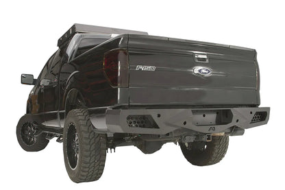 Fab Fours Vengeance rear bumper on a black Ford F-150, rear driver-side three-quarter studio view, showing the sculpted bumper, honeycomb corner vents and hitch receiver