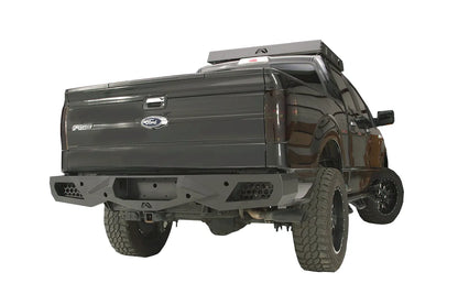 Fab Fours Vengeance rear bumper on a black Ford F-150, rear passenger-side three-quarter studio view, showing the sculpted rear bumper, honeycomb corner vents and center hitch opening