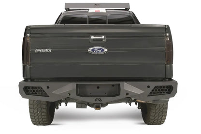 Fab Fours Vengeance rear bumper on a black Ford F-150, straight-on rear studio view, showing the sculpted bumper face, honeycomb corner vents and center hitch opening