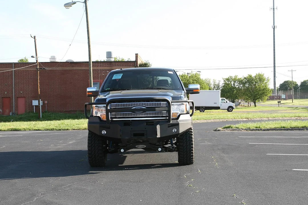 Fab Fours Premium Winch front bumper with full guard on a black Ford F-150, front view in a parking lot, showing the full grille guard, heavy-duty bumper face and fog lights