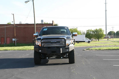Fab Fours Premium Winch front bumper with full guard on a black Ford F-150, front view in a parking lot, showing the full grille guard, heavy-duty bumper face and fog lights