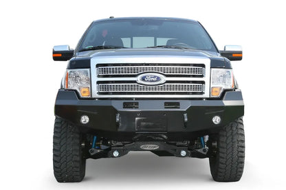 Fab Fours Premium Winch front bumper on a black Ford F-150, straight-on front view on a white background, showing the heavy-duty bumper face, winch opening and fog lights