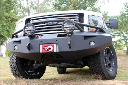 Fab Fours Premium Winch front bumper with pre-runner guard on a white truck, low close-up front view outdoors, showing the pre-runner hoop with mounted lights, winch fairlead and fog lights