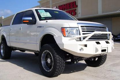 Fab Fours Premium Winch front bumper with pre-runner guard on a white Ford F-150, front passenger-side three-quarter view outdoors, showing the pre-runner hoop, bumper wing and fog lights