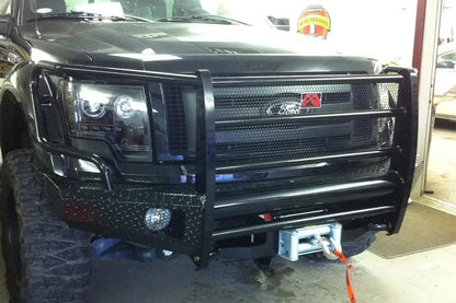Fab Fours Black Steel front ranch bumper with full guard on a black Ford F-150, close-up front view in a shop, showing the full grille guard, diamond-plate bumper and mounted winch