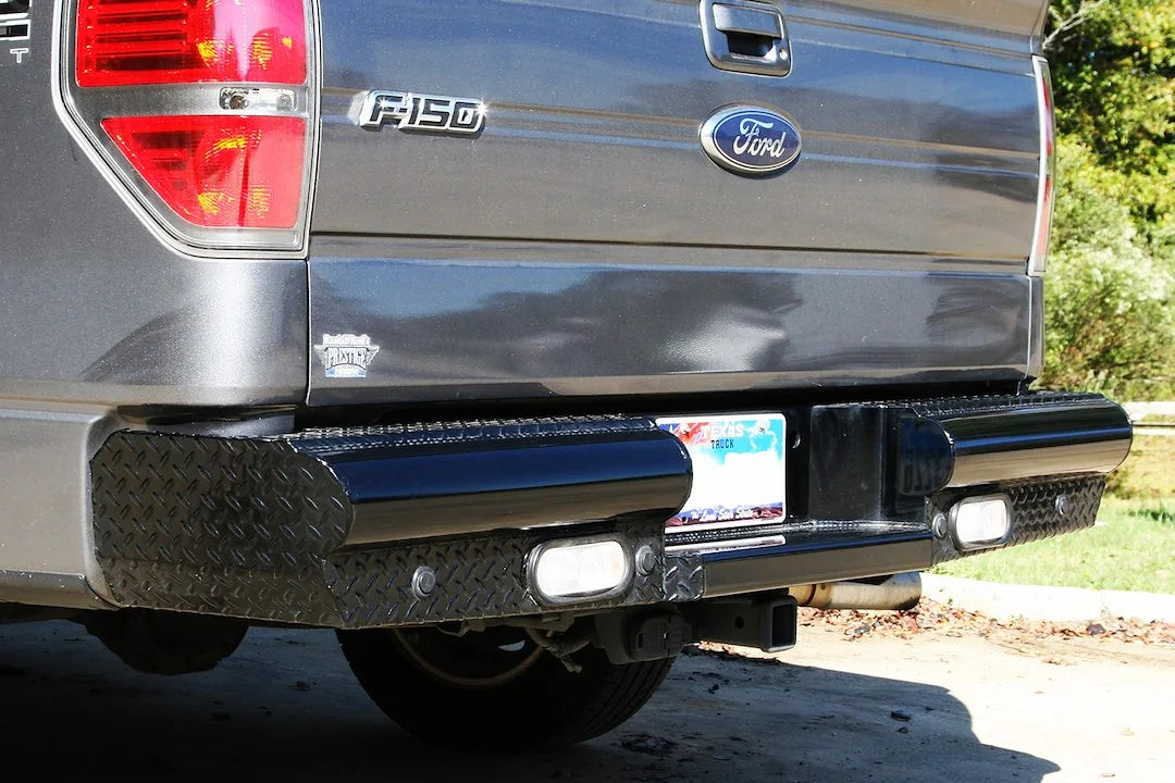 Fab Fours Black Steel ranch rear bumper on a gray Ford F-150, close-up rear view outdoors, showing the diamond-plate bumper wings, flush-mount lights and hitch receiver