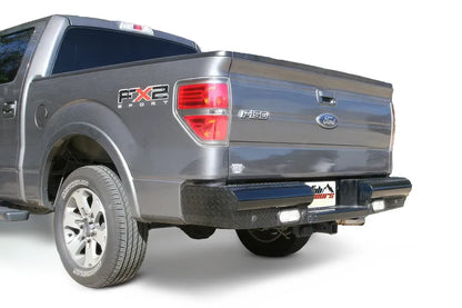 Fab Fours Black Steel ranch rear bumper on a gray Ford F-150, rear driver-side three-quarter view on a white background, showing the diamond-plate bumper, center plate pocket and flush-mount lights