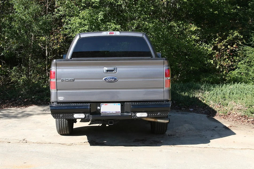 Fab Fours Black Steel ranch rear bumper on a gray Ford F-150, straight-on rear view outdoors, showing the diamond-plate rear bumper, center plate pocket and flush-mount lights