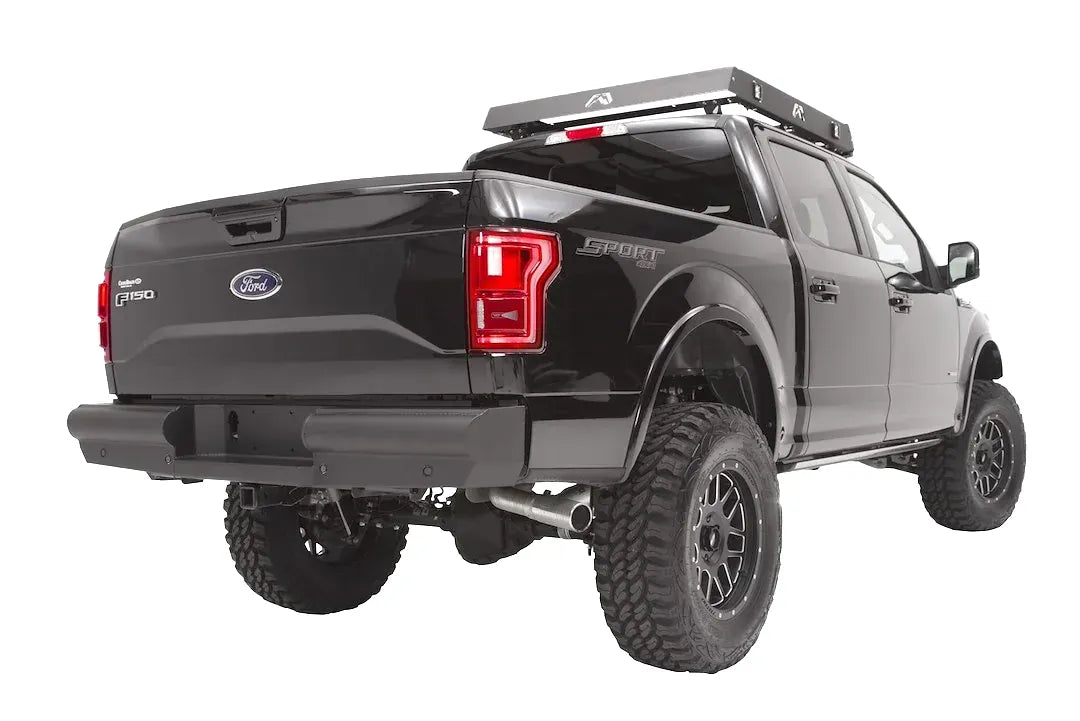 Fab Fours Black Steel Elite rear bumper on a black Ford F-150, rear driver-side three-quarter studio view, showing the smooth rear bumper, center plate pocket and hitch receiver
