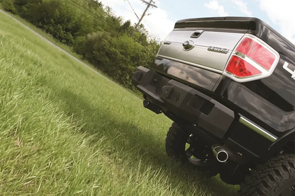 Fab Fours Premium rear bumper on a black Ford F-150, low angled close-up of the rear corner on a grassy slope, showing the heavy-duty bumper end, logo cutouts and hitch area