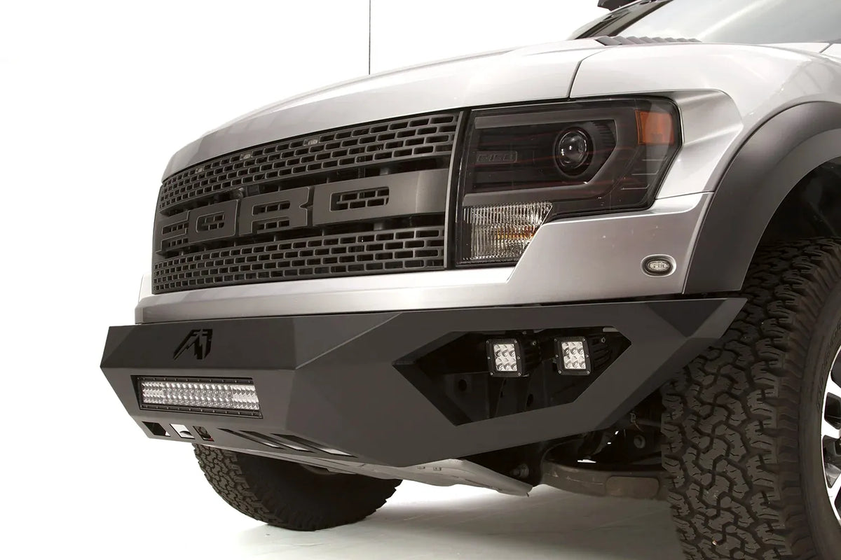 Fab Fours Vengeance front bumper on a silver Ford Raptor, close-up front view, showing the sculpted bumper face, center light bar and cube light pods