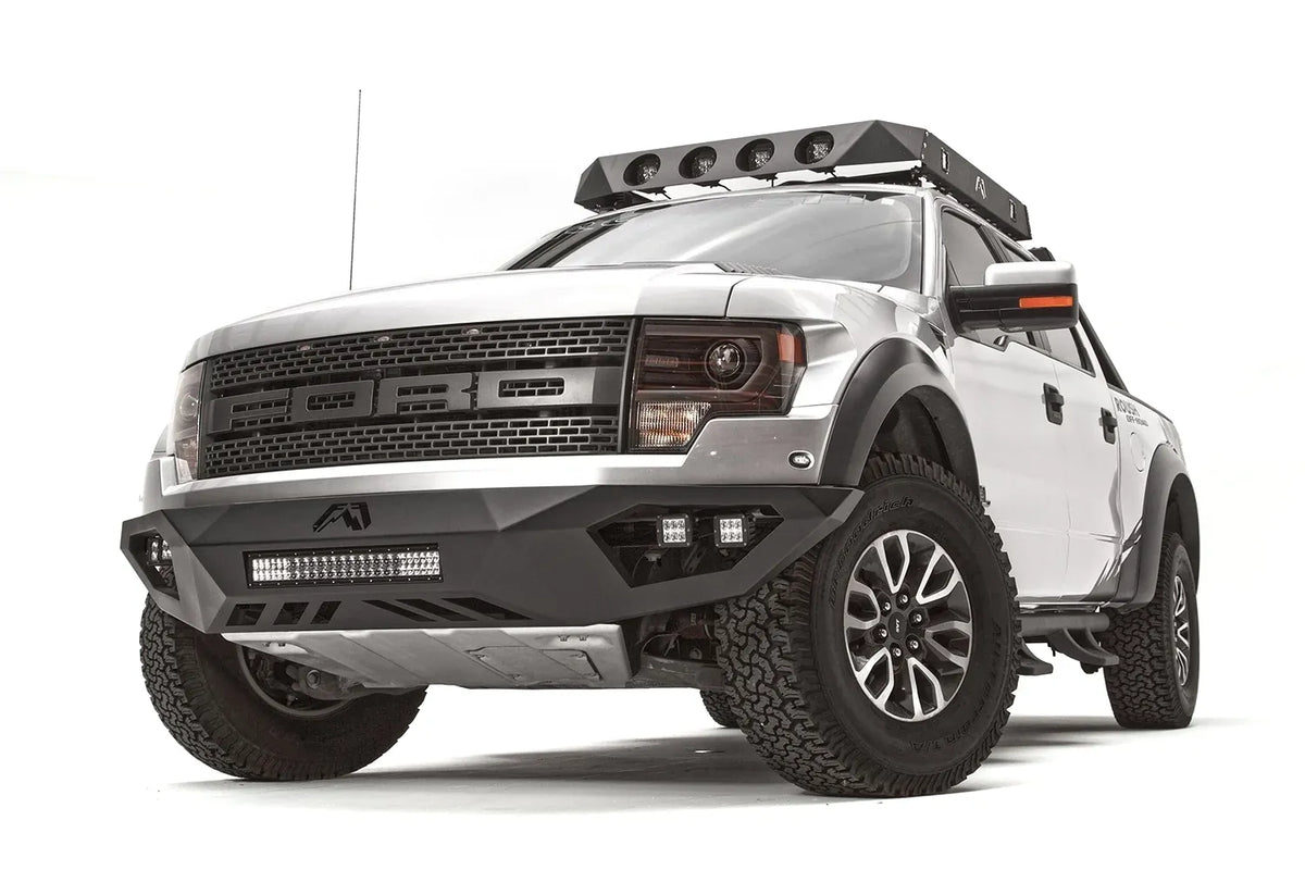 Fab Fours Vengeance front bumper on a silver Ford Raptor, front driver-side three-quarter studio view, showing the low-profile bumper, light bar and cube light pods