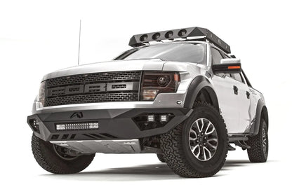 Fab Fours Vengeance front bumper on a silver Ford Raptor, front driver-side three-quarter studio view, showing the low-profile bumper, light bar and cube light pods