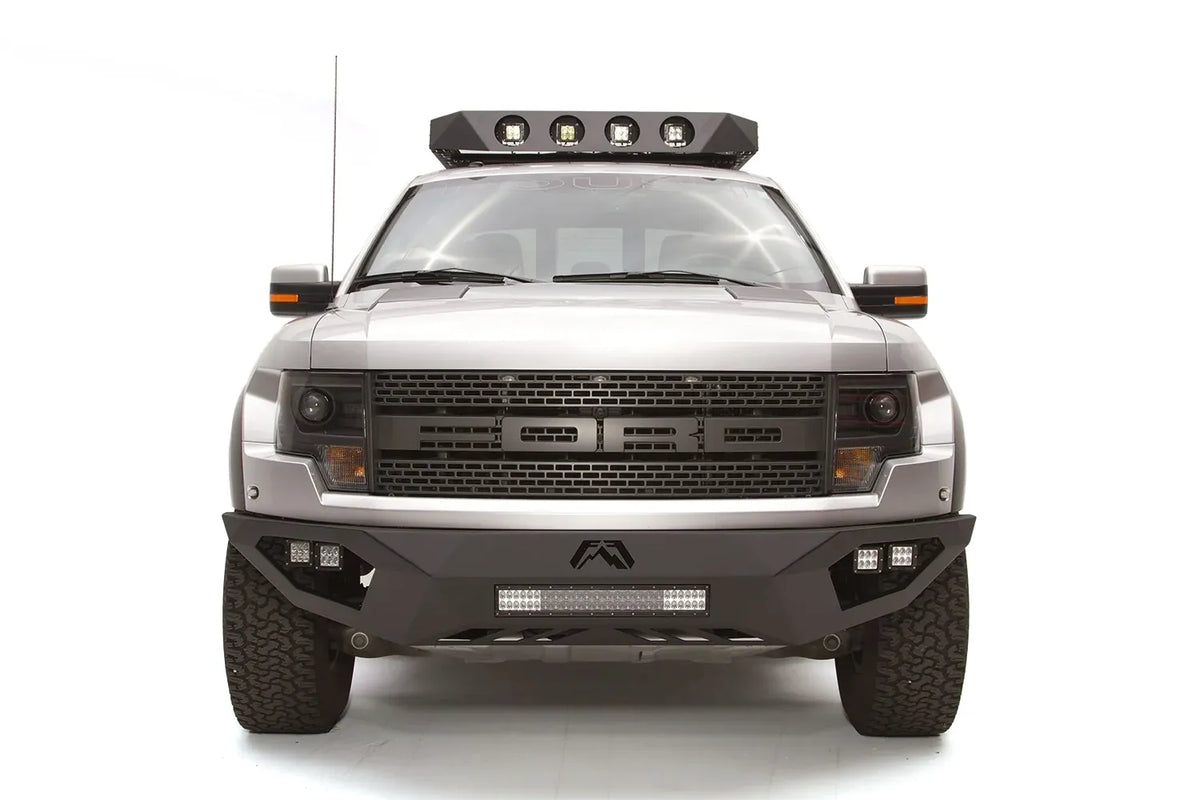 Fab Fours Vengeance front bumper on a silver Ford Raptor, straight-on front studio view, showing the sculpted bumper face, center light bar and cube light pods