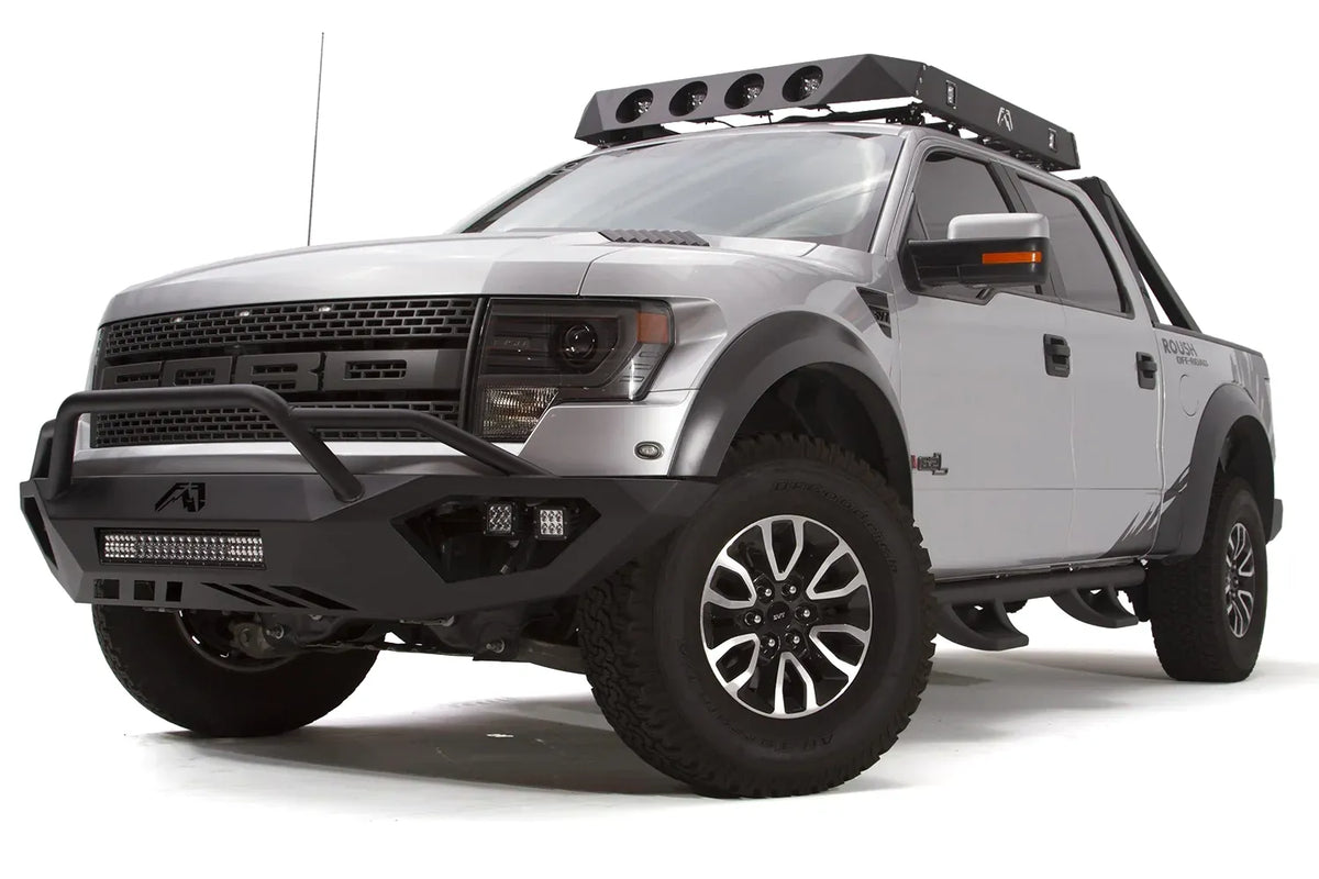 Fab Fours Vengeance front bumper with pre-runner guard on a silver Ford Raptor, front driver-side three-quarter studio view, showing the pre-runner hoop, light bar and cube light pods