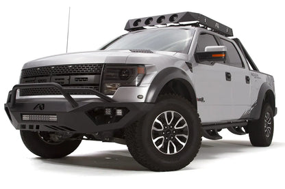 Fab Fours Vengeance front bumper with pre-runner guard on a silver Ford Raptor, front driver-side three-quarter studio view, showing the pre-runner hoop, light bar and cube light pods