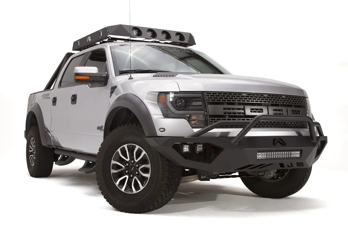 Fab Fours Vengeance front bumper with pre-runner guard on a silver Ford Raptor, front passenger-side three-quarter studio view, showing the pre-runner hoop, light bar and cube light pods