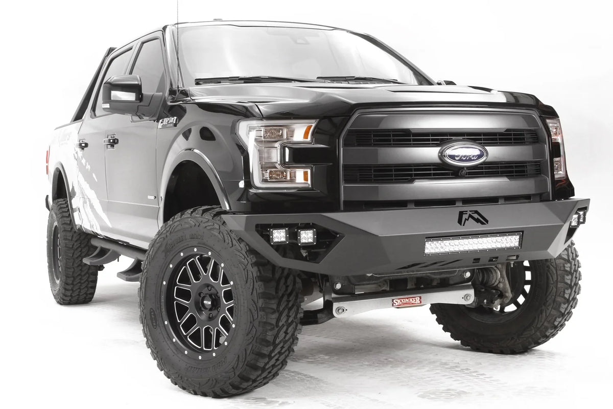 Fab Fours Vengeance front bumper on a black Ford F-150, front passenger-side three-quarter studio view, showing the sculpted bumper face, center light bar and cube light pods