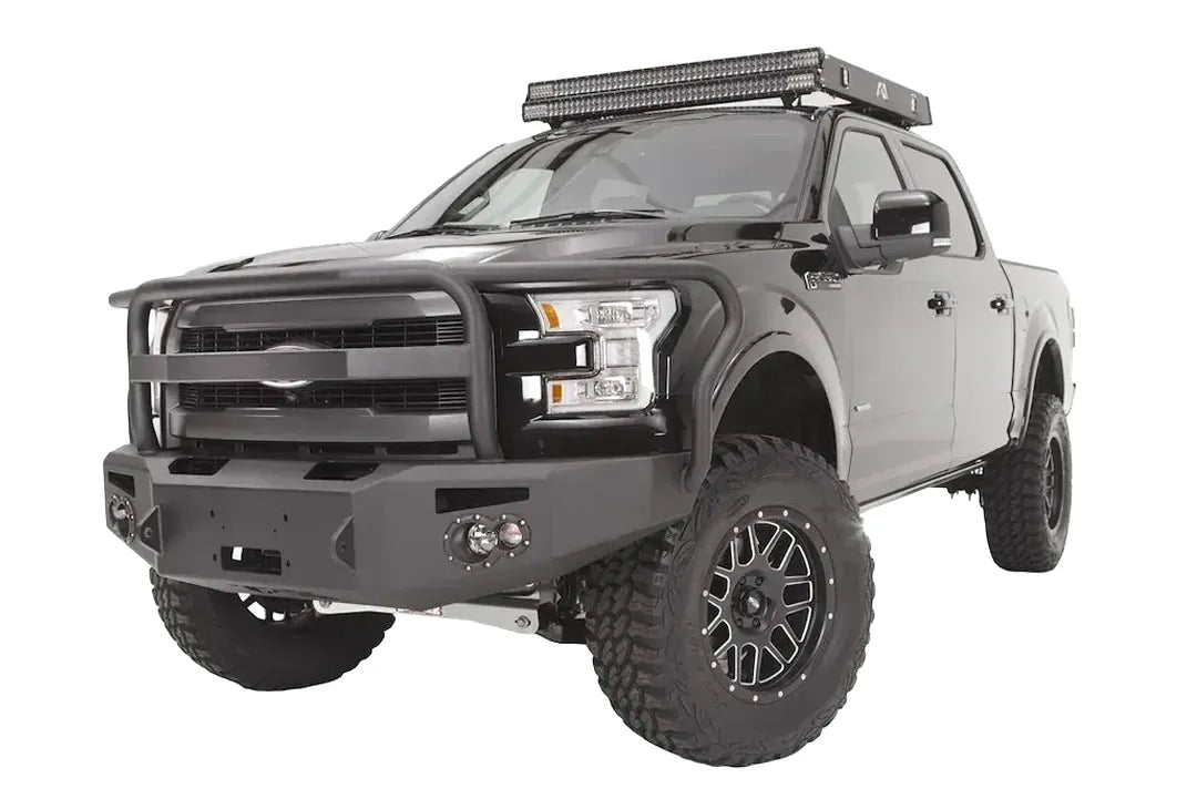 Fab Fours Premium Winch front bumper with full guard on a black Ford F-150, front driver-side three-quarter studio view, showing the full grille guard, heavy-duty bumper and round fog lights