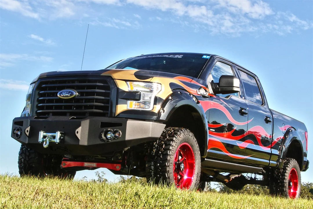 Fab Fours Premium Winch front bumper on a black Ford F-150 with flame graphics, front driver-side three-quarter view outdoors, showing the heavy-duty bumper, mounted winch and round fog lights