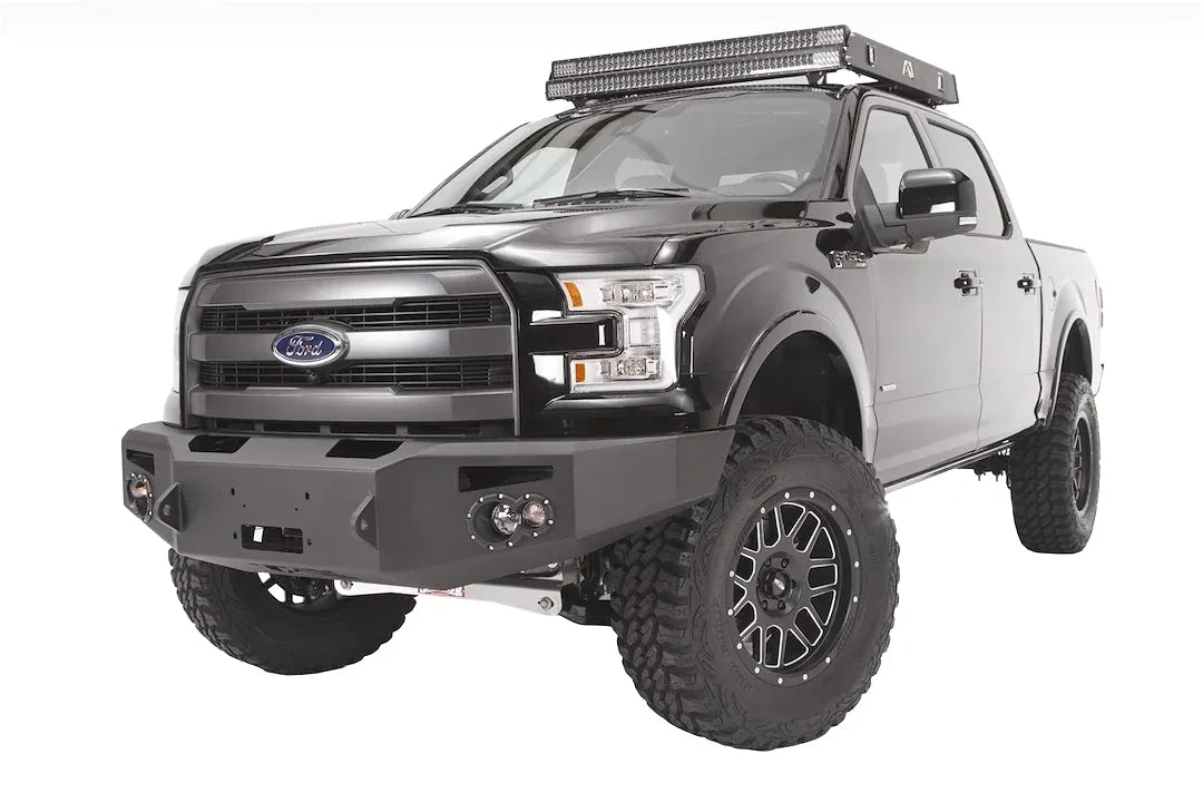 Fab Fours Premium Winch front bumper on a black Ford F-150, front driver-side three-quarter studio view, showing the heavy-duty bumper, winch-ready center section and round fog lights