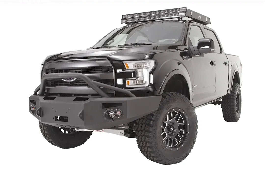 Fab Fours Premium Winch front bumper with pre-runner guard on a black Ford F-150, front driver-side three-quarter studio view, showing the pre-runner hoop, heavy-duty bumper and round fog lights