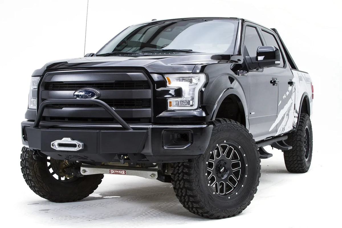 Fab Fours winch mount on a black Ford F-150, front driver-side three-quarter studio view, showing the pre-runner hoop, winch fairlead and low-profile front plate