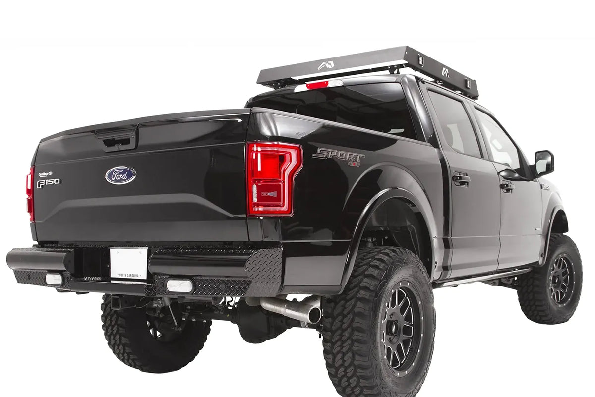 Fab Fours Black Steel rear bumper on a black Ford F-150, rear passenger-side three-quarter view, showing the diamond-plate end caps, rectangular lights and roof rack