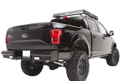 Fab Fours Black Steel rear bumper on a black Ford F-150, rear passenger-side three-quarter view, showing the diamond-plate end caps, rectangular lights and roof rack